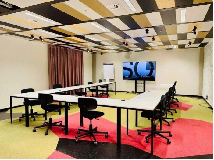 Salle de formation en U, écran de présentation et tapis colorés.