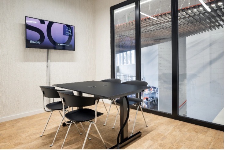 Petite salle de réunion vitrée, table pour quatre et écran mural.